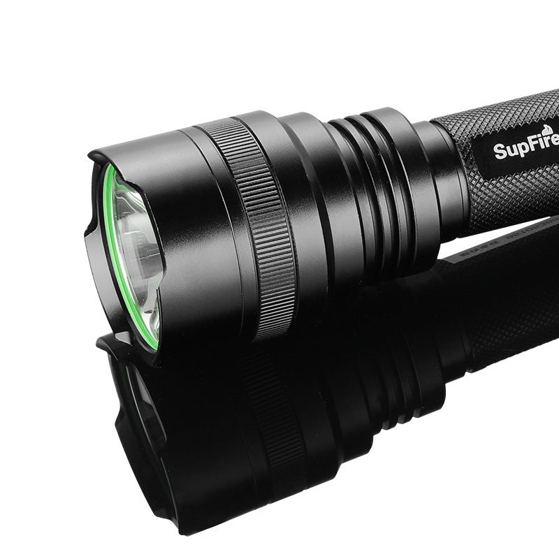 Close-up of a high-powered rechargeable LED flashlight with black textured body and green lens ring on reflective surface